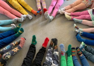 Kolorowe skarpetki na stopach dzieci siedzących w kole na dywanie.