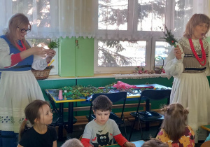Dzieci siedzą przy stolikach, wykonują palemki wielkanocne, Panie z Koła Ludowego pomagają Dzieciom w wykonaniu palemek.