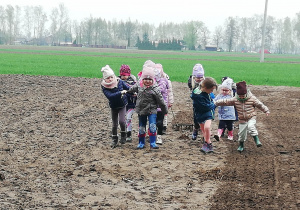 Dzieci na polu bronują ziemię.