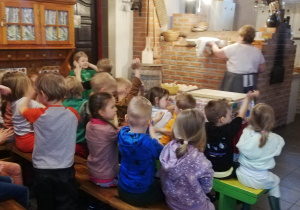 Dzieci siedzą w kuchni, oczekując na wypiek chleba.