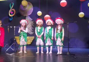 Grupa dzieci stoi na scenie, przed mikrofonami i śpiewa piosenkę o Łodzi.