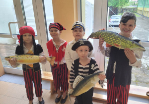Grupa chłopców przebranych za piratów stoi, trzymając sylwety ryb.