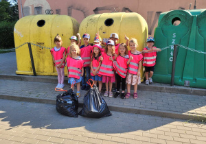 Dzieci stoją przy śmietnikach z workami zebranych śmieci.
