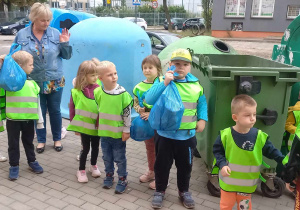 Dzieci stoją z workami śmieci przy koszach na śmieci.