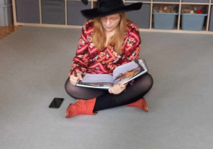 Autorka książki siedzi na dywanie.