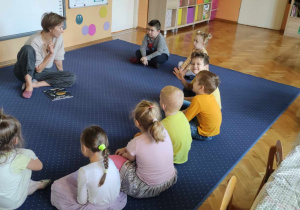 Dzieci z grupy Biedronki leżą z ilustratorką w kole na dywanie.