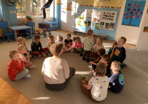 Dzieci z grupy Motylki siedzą z ilustratorką w kole na dywanie.