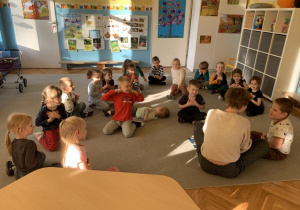 Dzieci z grupy Motylki siedzą z ilustratorką w kole na dywanie.