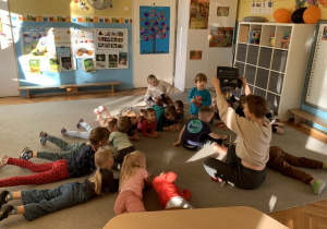 Dzieci z grupy Motylki leżą z ilustratorką w kole na dywanie.