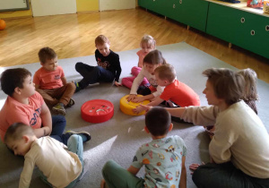 Dzieci z grupy Liski siedzą z ilustratorką w kole na dywanie.