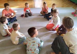 Dzieci z grupy Liski siedzą z ilustratorką w kole na dywanie.