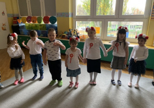 Dzieci stoją w kole, ubrane na galowo, śpiewają hymn Polski.
