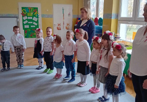 Dzieci stoją w kole, ubrane na galowo, śpiewają hymn Polski