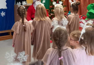 Dzieci z grupy Żabki stoją przed Mikołajem na tle dekoracji świątecznej.