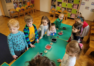 Dzieci stoją dookoła stołów, komponując swoje napoje herbaciane.