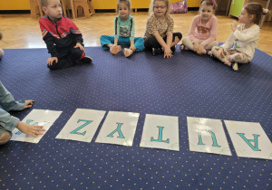 Dzieci z grupy Biedronki siedzą na dywanie z napisem "AUTYZM".