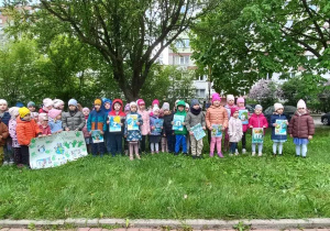 Przedszkolaki stoją w ogrodzie przedszkolnym z plakatem o Ziemi, śpiewają piosenkę.