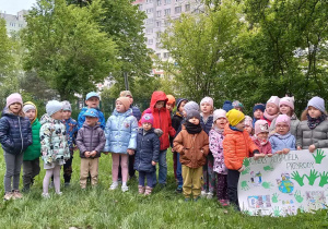 Przedszkolaki stoją w ogrodzie przedszkolnym z plakatem o Ziemi, śpiewają piosenkę.