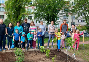 Rodzice, dzieci oraz kadra Przedszkola stoją przed ogródkiem owocowo - warzywnym.