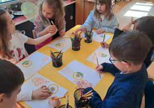 Dzieci siedzą przy stoliku i malują plakat pszczół.