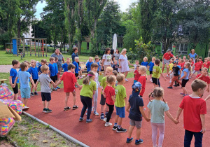 Dzieci i nauczyciele tańczą na boisku.