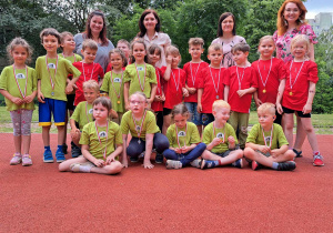 Grupa dzieci - zawodników sportowych stoi z nauczycielami na boisku.