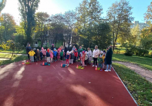 Dzieci stoją na boisku przedszklonym, uczestnicząc w zawodach sportowych.