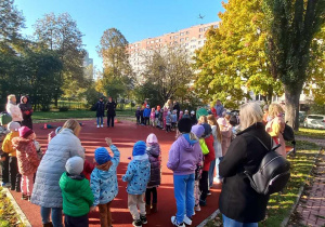 Dzieci stoją na boisku przedszklonym, uczestnicząc w zawodach sportowych.