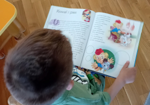 Chłopiec trzyma w rękach książkę, czytając.
