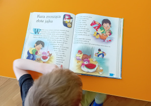 Chłopiec trzyma w rękach książkę, czytając.