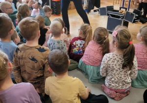 Iluzjonista pokazuje siedzącym dzieciom magiczne gadżety.