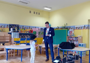 Iluzjonista pokazuje stojącej przed nim dziewczynce w czarnym kapeluszu kolorowe piłeczki w tubie.