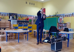 Iluzjonista trzyma w rękach czerwoną tubę, z której wyjmuje napój gazowany.