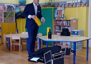 Iluzjonista prezentuje żółtą tubę, z której wyjął butelkę.