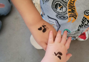 Rączki dzieci ze stempelkami nutek.