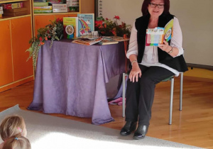 Dzieci siedzą na dywanie przed poetką Panią Urszulą Kowalską, która czyta dzieciom swoje utwory.