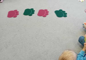 Na dywanie siedzą dzieci, wokół sylwet psich łapek.