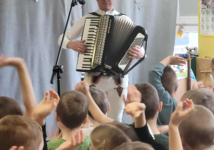 Góral Szczepan gra kolędy na akordeonie przed stojącymi dziećmi.