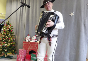 Góral Szczepan gra kolędy na akordeonie na tle dekoracji świątecznej.