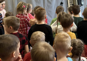 Góral Szczepan gra kolędy na akordeonie przed stojącymi dziećmi.