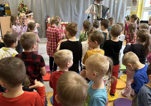 Góral Szczepan gra kolędy na akordeonie przed stojącymi dziećmi.