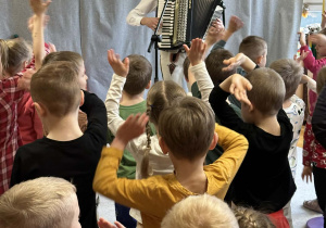 Góral Szczepan gra kolędy na akordeonie przed tańczącymi dziećmi.