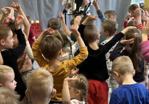 Góral Szczepan gra kolędy na akordeonie przed tańczącymi dziećmi.
