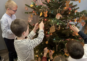 Dzieci ubierają choinkę w piernikowe ozdoby w szatni przedszkola.