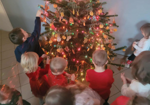 Dzieci ubierają choinkę w piernikowe ozdoby w szatni przedszkola.