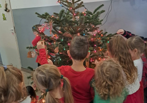 Dzieci ubierają choinkę w piernikowe ozdoby w szatni przedszkola.