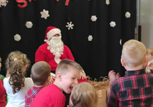 Dzieci stoją przed Mikołajem, oczekując na prezenty.