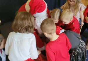 Dzieci wspólnie z Mikołajem oglądają swoje prezenty.