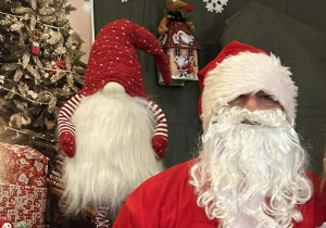 Mikołaj siedzi na krześle na tle świątecznej dekoracji.