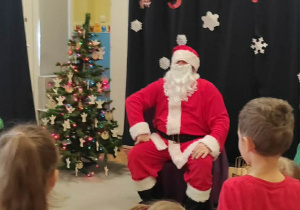 Dzieci stoją przed Mikołajem, oczekując na prezenty.